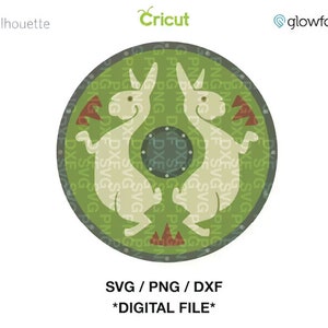 Puede incluir: Un diseño digital circular con dos conejos color crema enfrentados sobre un fondo verde. El diseño incluye detalles en rojo y marrón y el texto "SVG / PNG / DXF *ARCHIVO DIGITAL*". También están presentes los logotipos de Silhouette, Cricut y Glowforge.