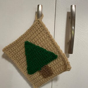 May include: A crocheted brown pot holder with a green and brown tree design.