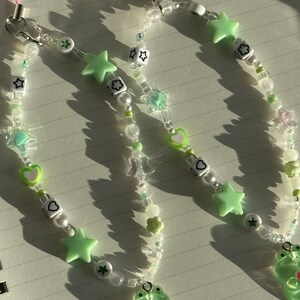 May include: Two green frog charm phone straps with white and green beads, stars, hearts, and flowers.