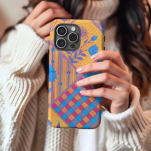 Può includere: Una custodia per telefono di colore giallo, blu e rosa con un design a scacchi. La custodia ha un ritaglio per la fotocamera ed è progettata per uno smartphone.