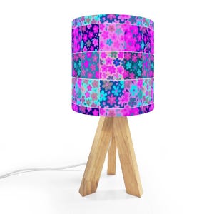 May include: A small table lamp with a floral patterned lampshade. The shade features a patchwork design with pink, blue, and purple flowers. The lamp has a natural wood tripod base and a white power cord.