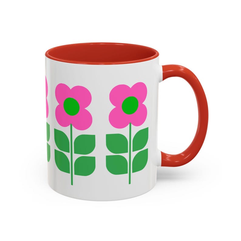 A white mug with a red handle, featuring a repeating pattern of pink flowers with green leaves.
