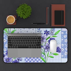 Puede incluir: Un tapete de escritorio con estampado floral azul y blanco con un portátil, un ratón y una taza de café encima.