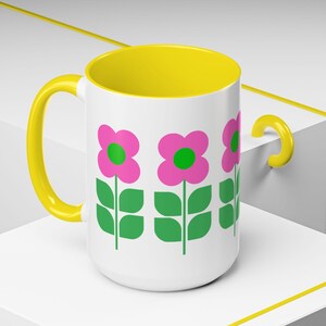 A white mug with a yellow handle and a floral design featuring pink flowers and green leaves.