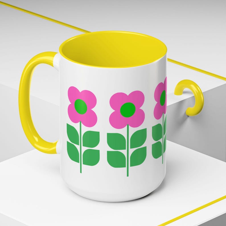 A white mug with a yellow handle and a floral design featuring pink flowers and green leaves.