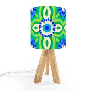 May include: A small table lamp with a colorful, patterned lampshade. The shade features a vibrant design in shades of blue, green, and white. The lamp has a wooden tripod base and a white power cord.
