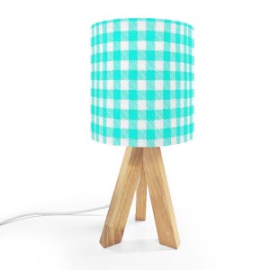 May include: A small table lamp with a turquoise and white checkered lampshade. The lampshade sits atop a natural wood tripod base. The lamp has a white power cord.