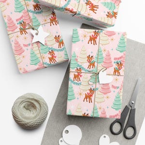 May include: Wrapping paper with a repeating pattern of brown reindeer wearing red or green scarves, interspersed with pink, mint green, and cream-colored Christmas trees, gold starbursts, and blue pine branches on a light pink background.
