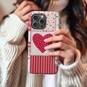 May include: A red, white, and pink patchwork phone case with a large red heart in the center. The heart has white polka dots. The case has a camera cutout and a cutout for the phone's buttons.