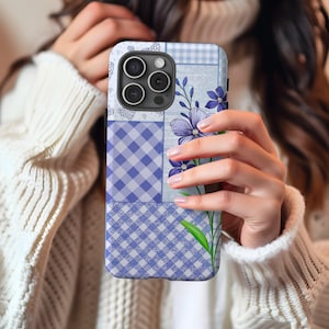 Può includere: Una custodia per telefono blu e bianca con fiori e design patchwork. La custodia ha un ritaglio per la fotocamera e un motivo floreale.