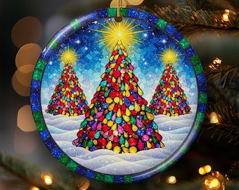 Puede incluir: Adorno navideño redondo con tres árboles de Navidad coloridos con estrellas en la parte superior. Los árboles están decorados con adornos vibrantes y de colores joya sobre un cielo azul estrellado. El adorno tiene un borde de mosaico y una cuerda dorada para colgar.