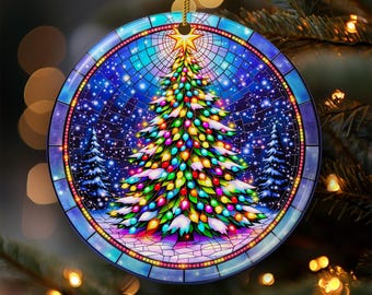 Puede incluir: Adorno navideño redondo con diseño de vidriera. El adorno presenta un árbol de Navidad decorado con luces de colores, nieve y dos árboles más pequeños. El fondo es un cielo estrellado. Se adjunta una cuerda dorada para colgarlo.