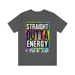 Pode incluir: Uma camiseta cinza escura com um design tie-dye e o texto "Straight Outta Energy #Pre-K Life" em branco.