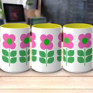 Three white mugs with green and pink flower designs on a wooden surface.