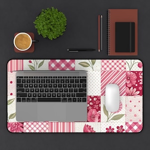 Può includere: Un tappetino per mouse con design patchwork rosa e bianco con un laptop, un mouse e una tazza di caffè su una scrivania nera.