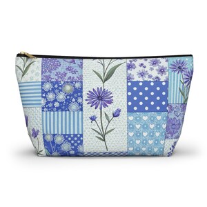 May include: A zippered cosmetic bag with a patchwork design featuring various blue floral and patterned squares. The bag has a black zipper and a gold-colored zipper pull. The bag is approximately 9 inches wide and 6 inches tall.