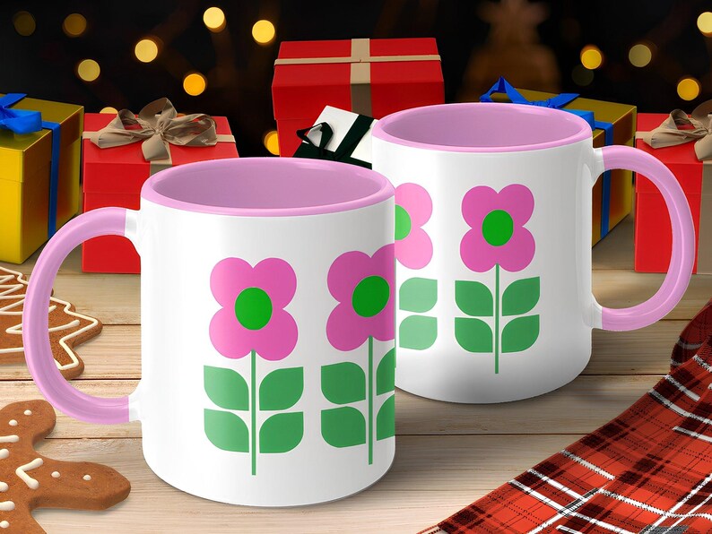 A pair of pink and white mugs with green flower designs, placed on a wooden surface with a gingerbread cookie and wrapped gifts in the background.