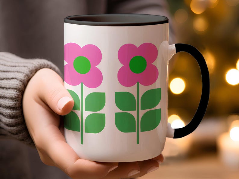 A person's hand holding a white mug with a floral design in pink and green colors.