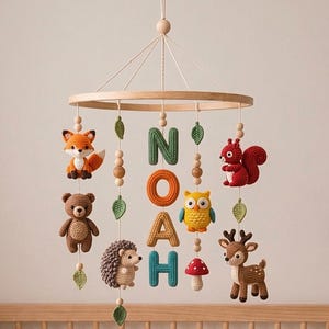 Pode incluir: Móvel de bebé artesanal com um anel de madeira, com animais da floresta de croché e o nome "NOAH" em letras coloridas. Inclui uma raposa, um urso, um esquilo, uma coruja, um veado, um ouriço e um cogumelo.