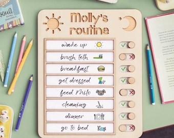 Puede incluir: Tabla de rutina diaria de madera con el texto "Molly's routine". La tabla incluye secciones para despertar, cepillarse los dientes, desayunar, vestirse, alimentar a Milo, limpiar, cenar y acostarse. Un sol y una luna están tallados.