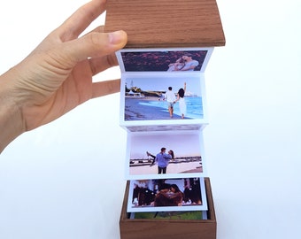 May include: A wooden box with a hinged lid opens to reveal a mini photo album with four photos of a couple on a beach and in a city setting.