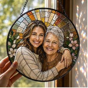 Puede incluir: Panel redondo de vidriera con un retrato de dos mujeres sonriendo y abrazándose. El panel tiene un marco de metal negro y una cadena para colgar. El fondo es un mosaico de colores cálidos, con acentos florales y de hojas.