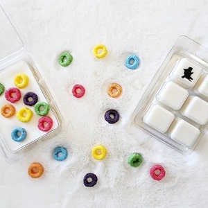 May include: A six-cube wax melt tray with a black silhouette of a person on the top cube. The tray is surrounded by colorful cereal rings on a white surface.