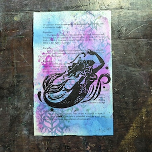 May include: An artwork featuring a black mermaid silhouette on a page of text. The background has a watercolour effect with blue, purple, and pink hues. The page is signed in the bottom right corner.