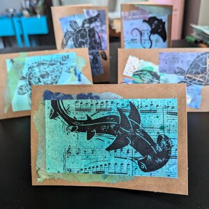 May include: Four brown cards with different images of sea creatures. The cards are decorated with blue and green watercolor washes. One card features a hammerhead shark, another features a turtle, and the other two feature a manta ray and a seahorse.