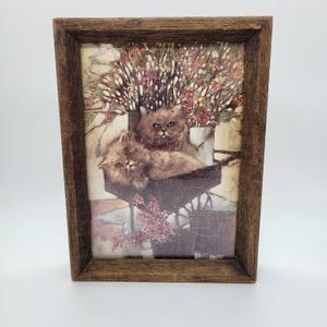 Puede incluir: Una taza de cerámica blanca con un asa negra y el texto "But First, Coffee" en negrita negra. La taza se encuentra sobre un fondo borroso, sugiriendo un ambiente acogedor.