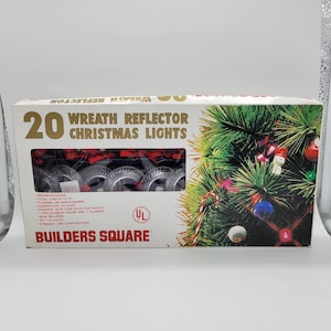 May include: A box of 20 Wreath Reflector Christmas Lights from Builders Square. The box features a Christmas tree design with ornaments and the text "20 Wreath Reflector Christmas Lights". The lights are 15 ft long and are suitable for indoor or outdoor use.