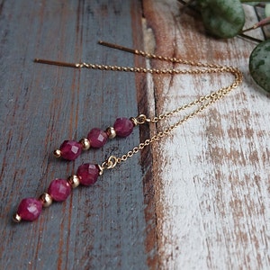 May include: A pair of gold chain earrings with a dangling row of five faceted, dark pink beads.