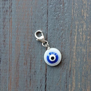 Op de afbeelding: Een zilveren bedel met een blauw en wit boze oog ontwerp. De bedel heeft een kreeft sluiting.