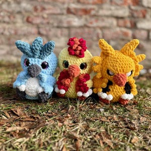 Puede incluir: Tres peluches de pájaros hechos a mano con ganchillo, alineados. Los pájaros son azules, amarillos y naranjas, con detalles en blanco y negro. Tienen grandes ojos brillantes y están sobre hierba.