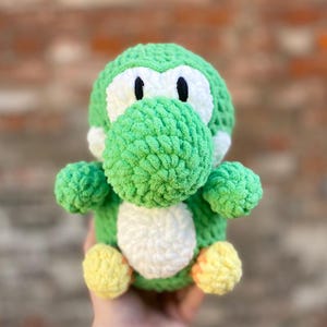 Può includere: Peluche Yoshi in crochet verde con occhi bianchi e pancia bianca. Il giocattolo ha accenti gialli sui piedi.
