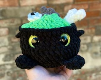May include: A black cauldron with green goo inside and a white bone sticking out. The cauldron has googly eyes and a cute expression.