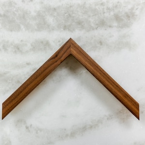 May include: A corner piece of a wood picture frame. The frame is made of a dark brown wood with a smooth finish.