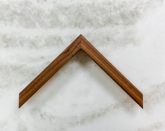 May include: A corner piece of a wood picture frame. The frame is made of a dark brown wood with a smooth finish.