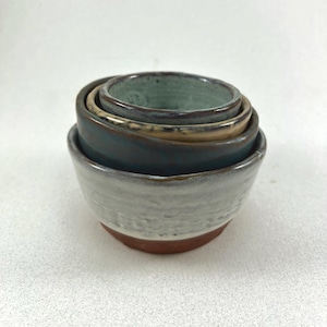 Puede incluir: Conjunto de cuatro cuencos encajables en varios tonos de azul, blanco y marrón. Los cuencos están hechos de cerámica y tienen un aspecto rústico y hecho a mano.