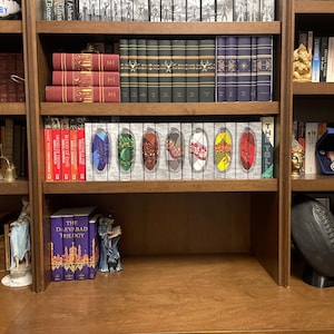 May include: A wooden bookshelf filled with various books. The shelves display rows of hardback books in different colors, including red, green, and blue. Decorative items like statues and a football are also visible.