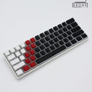 May include: A white and black keyboard with red keycaps. The keyboard has a black space bar and a black top row. The keyboard is labeled "KROME KEYCAPS".