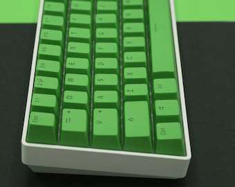 May include: A white and green mechanical keyboard with a green space bar and a green escape key. The keyboard has a white frame and is angled to the right. The keyboard is on a black surface.