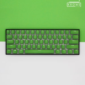 May include: A compact, black mechanical keyboard with bright green keycaps. The keyboard features a standard QWERTY layout with alphanumeric keys, function keys, and a space bar. The brand name "KROME KEYCAPS" is visible in the top right corner.