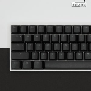 May include: A black mechanical keyboard with white keycaps and a white frame. The keys are labeled with the standard QWERTY layout. The keyboard has a space bar, a backspace key, an enter key, and a shift key. The keyboard is on a black surface.