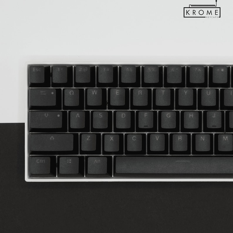 May include: A black mechanical keyboard with white keycaps and a white frame. The keys are labeled with the standard QWERTY layout. The keyboard has a space bar, a backspace key, an enter key, and a shift key. The keyboard is on a black surface.
