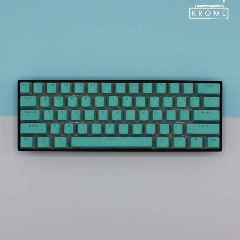 May include: A compact, black keyboard with teal keycaps. The keys are arranged in a standard QWERTY layout. The keyboard has a sleek, minimalist design, with the brand name "KROME KEYCAPS" in the top right corner.
