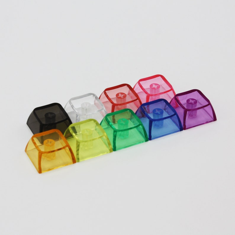 May include: Assortment of ten transparent keycaps in various colours, including black, white, yellow, green, blue, purple, and red. The keycaps are made of a clear plastic material and have a slightly raised edge around the perimeter.