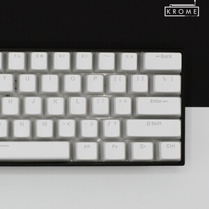 May include: A white mechanical keyboard with a black frame. The keyboard has a standard layout with keys labelled 7, 8, 9, 0, Y, U, I, O, P, H, J, K, L, ;, ', N, M, <, ., >, /, ?, Shift, Enter, Back, =, +, Alt, Fn, Ctrl. The keyboard is on a white surface.