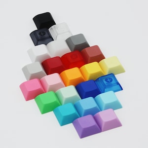 May include: A collection of colorful keycaps arranged in a pyramid shape. The keycaps are made of plastic and come in a variety of colors, including pink, blue, green, yellow, red, and orange.