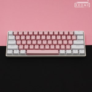 May include: A white and pink mechanical keyboard with a pink space bar and white keycaps. The keyboard has a pink and white color scheme and features the text "KROME KEYCAPS" in the top right corner.